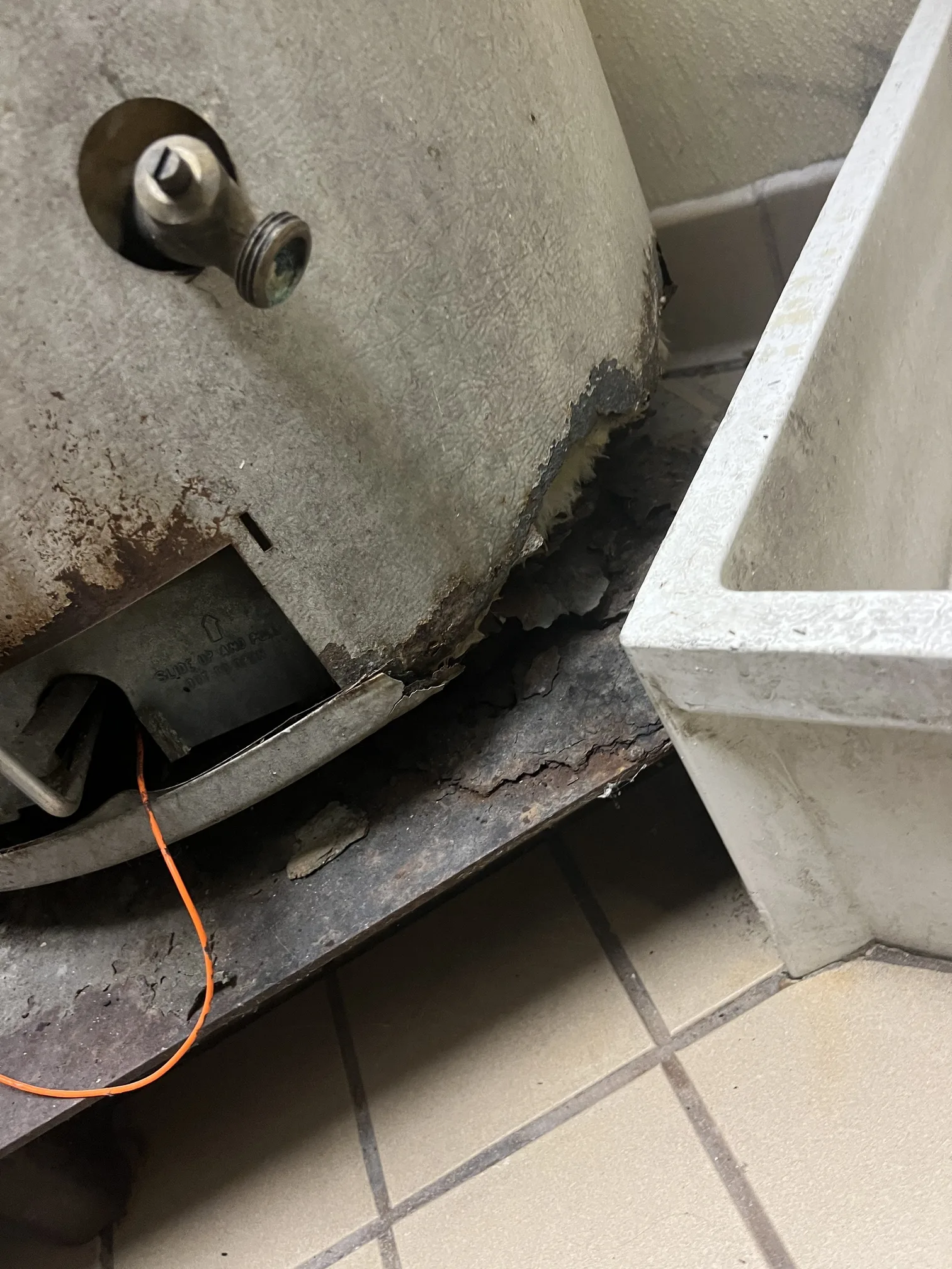 Corroded commercial water heater base showing deterioration requiring replacement